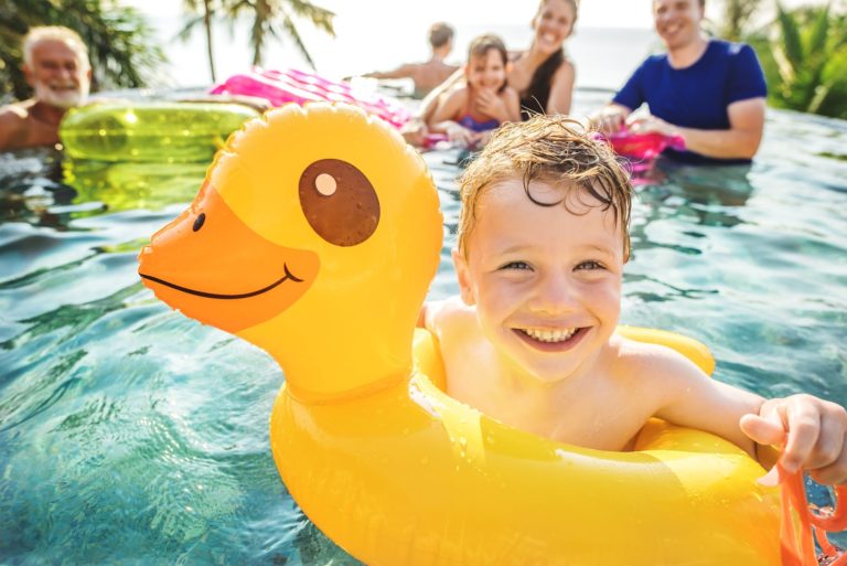 Smiling boy with rubber ducky float enjoys staycation with family in pool